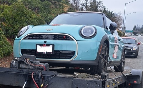 Light blue Mini Cooper on a tow truck, showcasing a decorative design. Relevant for discussions on vehicle recovery or automotive services.