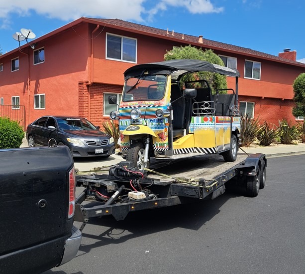 Colorful tuk-tuk loaded onto a trailer in front of a red building. The image showcases the vibrant design and highlights transportation culture.