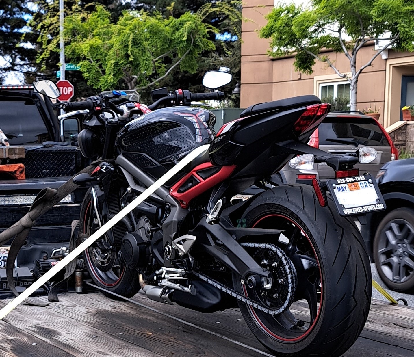 Sport motorcycle parked on a truck bed, showcasing its sleek black and red design. A stop sign and trees are visible in the background, indicating an urban setting.